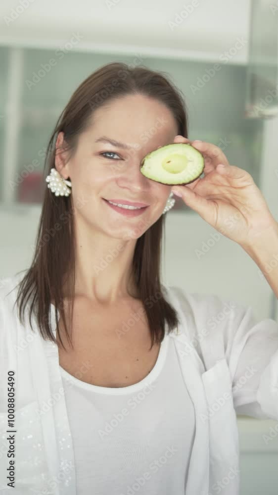 A young beautiful girl brings half an avocado to her eye and shows the gesture with her fingers ok. A young beautiful girl brings half an avocado to her eye and shows the gesture with her fingers ok.