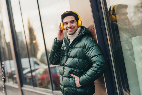 Photo of cheerful smiling attractive man listening music modern device walking city street on weekend photo