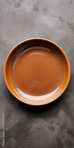 A brown bowl with a clear base sits on a grey countertop. The bowl is empty and he is a decorative piece