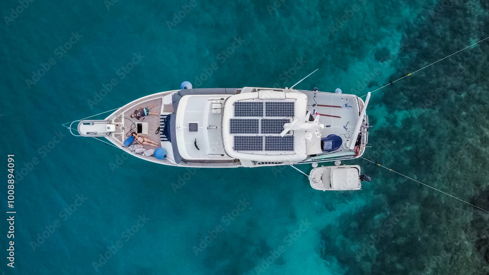 Fototapeta premium Aerial view from above of a large eco-friendly yacht with solar panels receiving energy during the day in the sea with clear, blue water. In the Mediterranean Sea. two persons in it. View from drone.