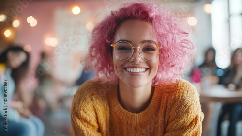 A woman with bright pink hair and glasses, smiling warmly in a cozy café setting, surrounded by blurred backgrounds of people and lights. photo