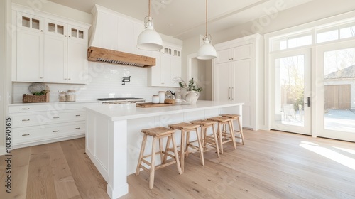 A modern kitchen featuring an island with wooden stools, stylish pendant lights, and sleek cabinetry, all illuminated by large glass doors and windows.