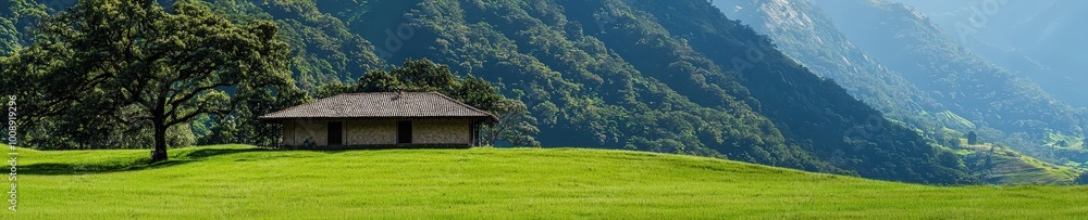 Naklejka premium A peaceful landscape featuring a solitary house nestled in lush green grass, surrounded by majestic mountains and trees under a clear blue sky.