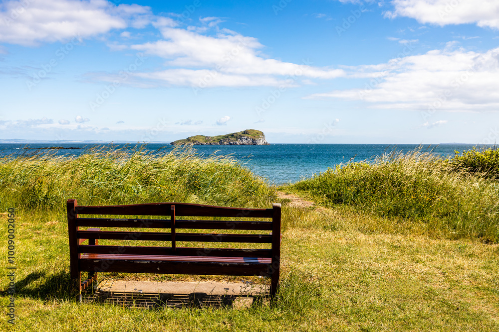 Serene Beachside Bench, bringing Solitude by the Sea through an empty bench with a view of Craigleith Island, North Berwick on a sunny day, Scotland, UK, 2024-29-06: Serene Beachside Bench, bringing Solitude by the Sea through an empty bench with a view of Craigleith Island, North Berwick on a sunny day, Scotland, UK, 2024-29-06: