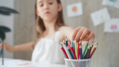 Close-up of a child's hand picking a pencil from a colorful set for a creative activity. Young girl choosing colored pencils