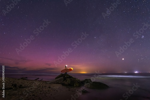 Canvas Print surfer with board on beach at night under starry sky and aurora borealis