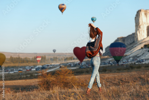 Woman in denim jeans and backpack standing in front of a field with hot air balloons in the background