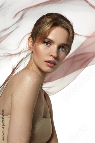 Portrait of a beautiful young woman with natural makeup and smooth skin, against the background of soft flowing fabric. The image emphasizes tenderness and lightness, creating a romantic mood. 
