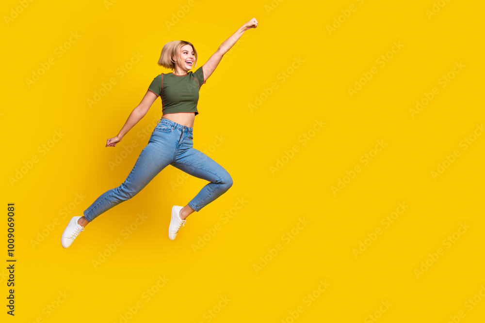 Full size photo of lovely girl dressed khaki crop top jeans fly raising fist up look empty space isolated on yellow color background Full size photo of lovely girl dressed khaki crop top jeans fly raising fist up look empty space isolated on yellow color background