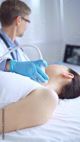 Doctor man wearing blue protective gloves is using ultrasound equipment on the neck of a patient woman, lying for examination. Medicine concept