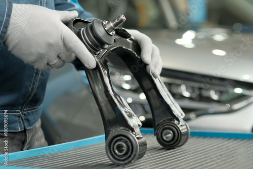 Car repair at a car service center. An auto mechanic holds the front suspension lever in his hands. Inspection and control of the serviceability of a new part before replacing a faulty suspension arm.