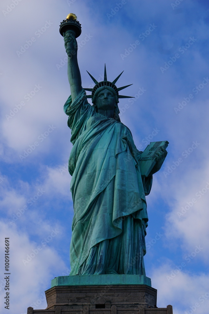 Fototapeta premium Vertikale, frontale Ansicht der berühmten Freiheitsstatue von New York, die vor klarem blauen Himmel die Fackel der Freiheit in die Luft streckt