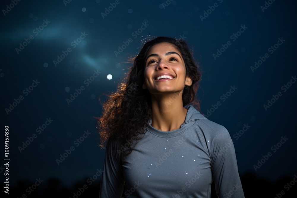 Portrait of a joyful indian woman in her 20s showing off a lightweight base layer isolated in sparkling night sky Portrait of a joyful indian woman in her 20s showing off a lightweight base layer isolated in sparkling night sky