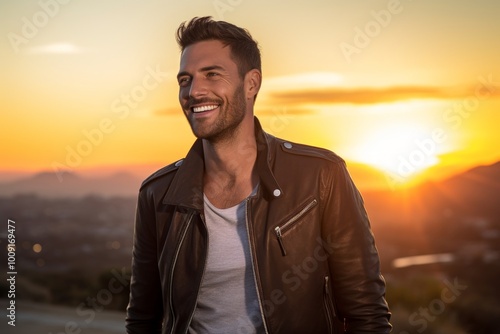 Portrait of a smiling man in his 30s sporting a stylish leather blazer in front of vibrant sunset horizon