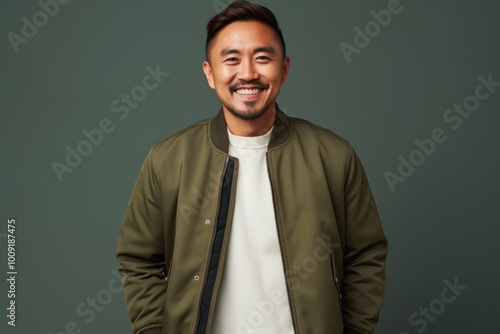 Portrait of a happy asian man in his 40s sporting a stylish varsity jacket isolated in modern minimalist interior