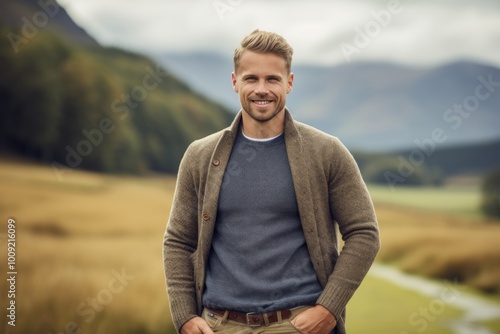 Portrait of a smiling man in his 30s wearing a chic cardigan over quiet countryside landscape