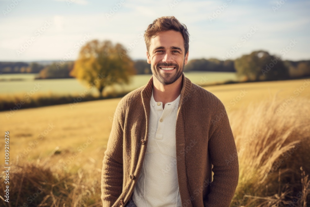 Portrait of a smiling man in his 30s wearing a chic cardigan in front of quiet countryside landscape Portrait of a smiling man in his 30s wearing a chic cardigan in front of quiet countryside landscape