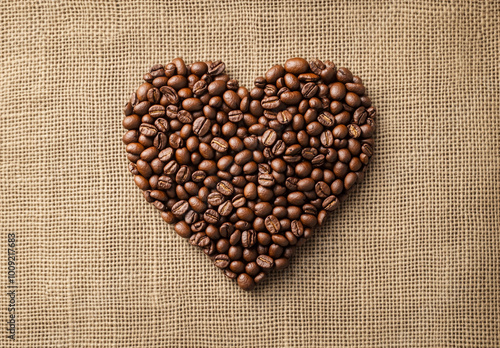 A heart-shaped arrangement made of coffee beans on a burlap background. 