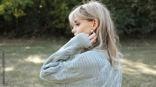 Attractive young blonde woman in a gray sweater and black skirt walks through the autumn park and enjoys the warm autumn weather