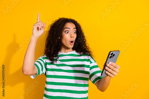 Photo of pretty young girl smart phone point finger wear striped t-shirt isolated on yellow color background