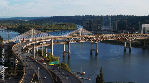 Breathtaking aerial footage of the Willamette River, Portlands skyline and iconic Tilikum Crossing, Bridge of the People at sunset, city lights, traffic and moving cars on the freeway interchange. photo