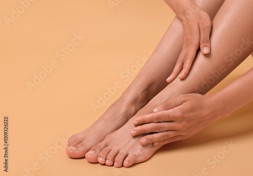 Woman touching her smooth feet on beige background, closeup