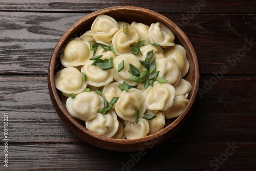 Delicious pelmeni with green onion in bowl on wooden table, top view photo