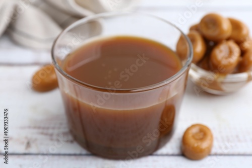 Tasty caramel sauce in bowl and candies on white wooden table, closeup