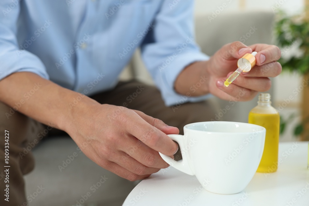 Young man dripping CBD tincture into drink at white table, closeup Young man dripping CBD tincture into drink at white table, closeup