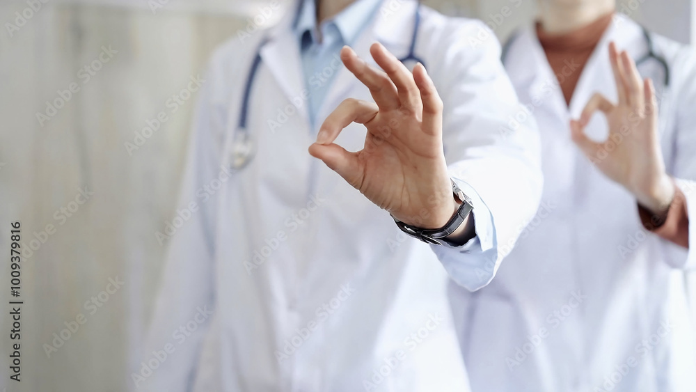 Two doctors is showing ok sign with fingers while standing in a hospital. Teamwork and success in medicine Two doctors is showing ok sign with fingers while standing in a hospital. Teamwork and success in medicine