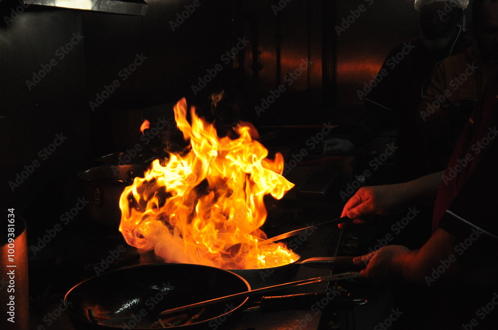 Chef cooking in the kitchen stove with flamed fire on a pan. Closeup ...