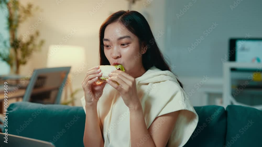Young woman enjoys a well-deserved break from work, relaxing on her couch while savoring a delicious sandwich. Comfort and satisfaction fill the cozy living room atmosphere Young woman enjoys a well-deserved break from work, relaxing on her couch while savoring a delicious sandwich. Comfort and satisfaction fill the cozy living room atmosphere