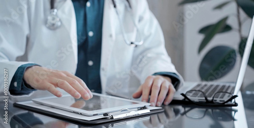 Doctor man wearing white medical coat over a green shirt is using tablet computer making some notes, close up of hands. Medicine and health care