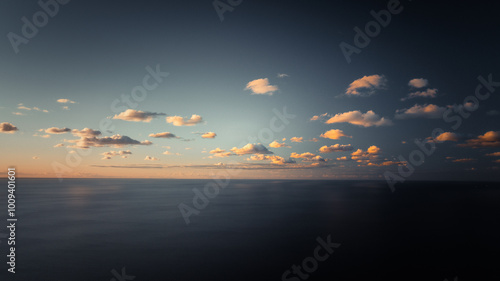  A sizable expanse of water dotted with clouds above, features a vessel afloat on its opposite side