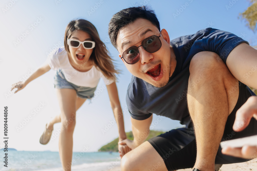 Playful asian couple lovers taking photo together at the beach, low angle. Playful asian couple lovers taking photo together at the beach, low angle.