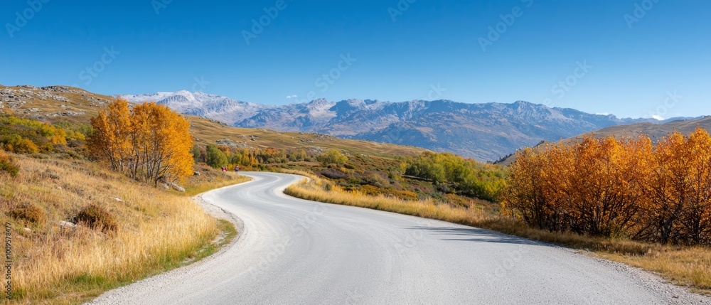 A road with a curved section, surrounded by a grassy area, leads to a mountain range in the background