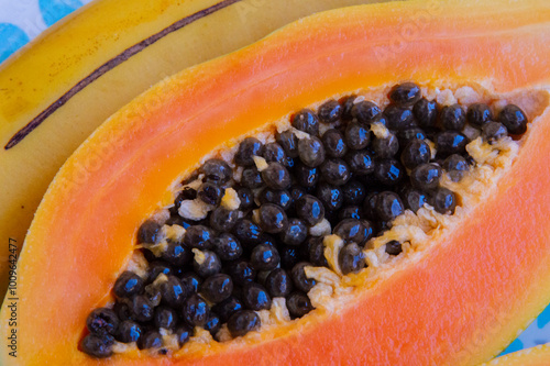 close-up: big orange hue ripe fruit of papaya cut in two with  large central cavity are attached numerous black seeds on a turquois blue plate with rhombus pattern photo