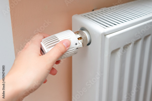 Woman regulates temperature at home with the heating knob on room battery. Metal radiator with individual control. heating system, energy crisis, energy saving, heat saving, heating season