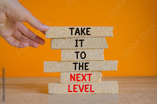 Concept words Take it to the next level on brick blocks. Businessman hand. Beautiful wooden table orange background. Business career path for growth and success concept.