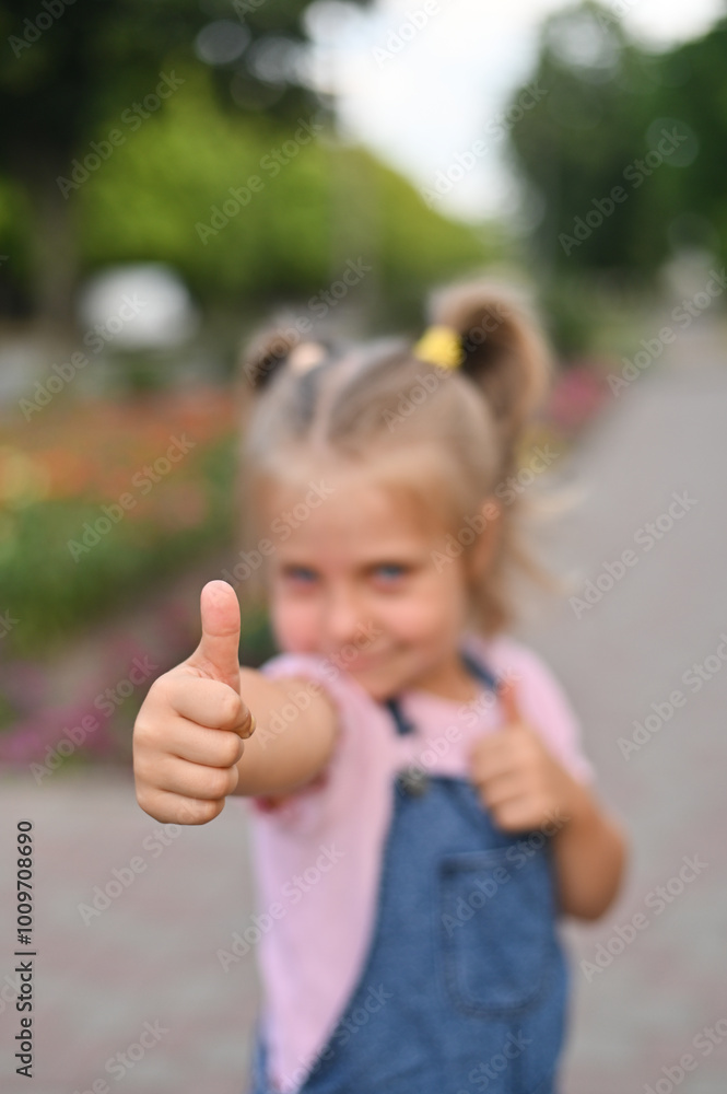 A sweet smiling girl stands with her thumb raised. The child shows thumbs up gesture A sweet smiling girl stands with her thumb raised. The child shows thumbs up gesture