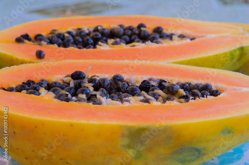 close-up: big orange hue ripe fruit of papaya cut in two with  large central cavity are attached numerous black seeds on a turquois blue plate with rhombus pattern