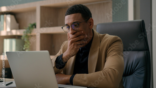 Upset frustrated male office worker African American ethnic businessman reading bad news on computer laptop confused business man worry anxiety difficulties loss money job failure problem bankruptcy