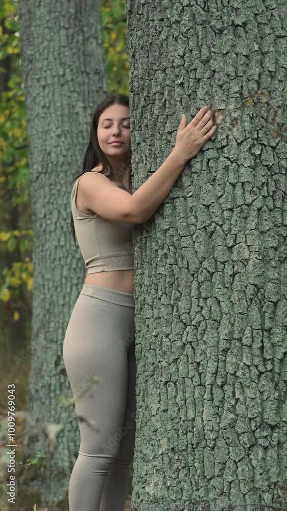 Smiling young woman embracing a tree with her eyes closed in a peaceful forest scene. Vertical video Smiling young woman embracing a tree with her eyes closed in a peaceful forest scene. Vertical video