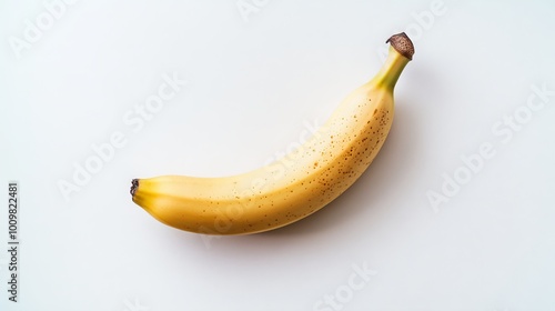 A ripe, yellow banana rests on a pristine white backdrop, its smooth, slightly wrinkled skin invitingly curved. The banana's slender form is a beacon of ripeness, its delicate speckles