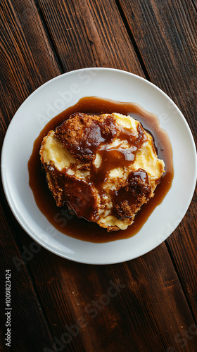 Delicious bread pudding dessert with caramel sauce on white plate and wooden table. Golden brown pastry contrasts beautifully. Perfect for any mealtime