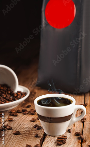 Cup of hot drink steaming. Spilled coffee beans from the white ceramic cup and black package on brown wooden background. Coffee shop, caffeine, roast concept. Roasted beans for mass market sale. photo