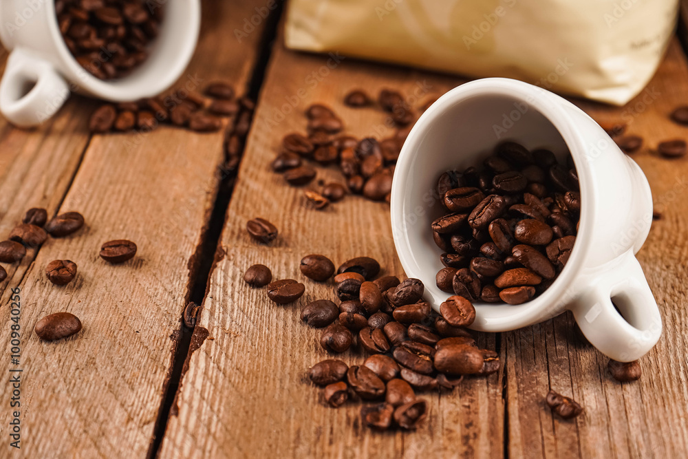 Roasted beans for mass market sale. Spilled coffee beans from two white ceramic cups on brown wooden background. Coffee shop, caffeine, roast concept. Roasted beans for mass market sale. Spilled coffee beans from two white ceramic cups on brown wooden background. Coffee shop, caffeine, roast concept.