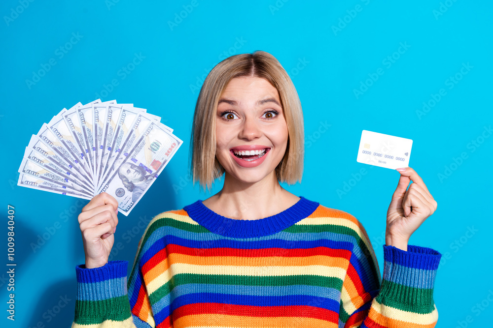 Photo portrait of pretty young girl hold money fan credit card wear trendy striped outfit isolated on blue color background Photo portrait of pretty young girl hold money fan credit card wear trendy striped outfit isolated on blue color background