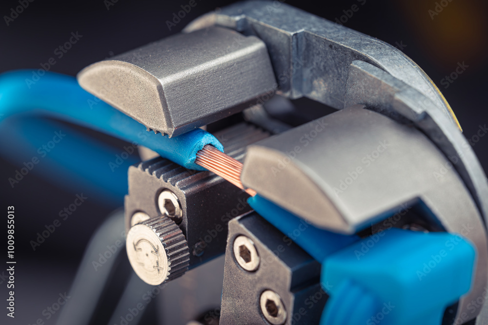 Close-up of a wire stripper tool cutting a blue wire with exposed copper. Macro shot of electrical equipment. Close-up of a wire stripper tool cutting a blue wire with exposed copper. Macro shot of electrical equipment.