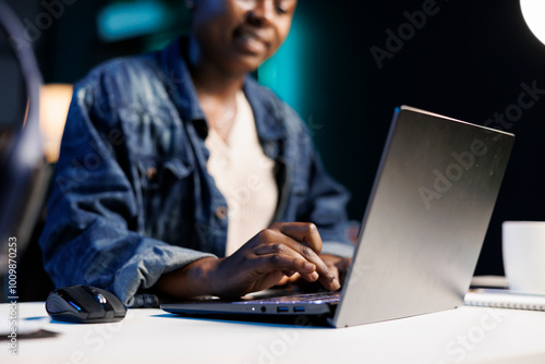 Close up of black woman at the desk typing on her personal computer, browsing the internet. African american freelancer using the laptop, answering emails, and working from home.